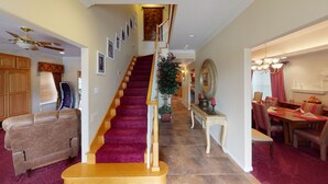 A staircase with a red carpet, wooden walls, a dining area with a chandelier, and a ceiling fan.