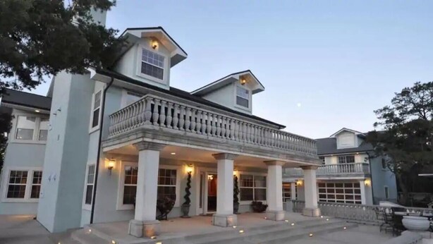 A large, two-story house with a balcony, columns, and a covered porch.