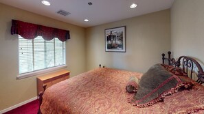 A bedroom with a large bed, a window with blinds, a bedside table, and a framed picture on the wall. - Exquisite Mountain Mansion West Wing (Silver City)