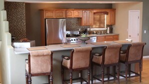 A kitchen with a central island, wooden bar stools, a stainless steel refrigerator, and a stove. - Exquisite Mountain Mansion West Wing (Silver City)