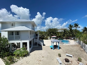 A two-story white house with a balcony, a pool area with umbrellas, and palm trees. - Luxury Oceanview Pool Eco-friendly Villa Near Key West (Summerland Key)
