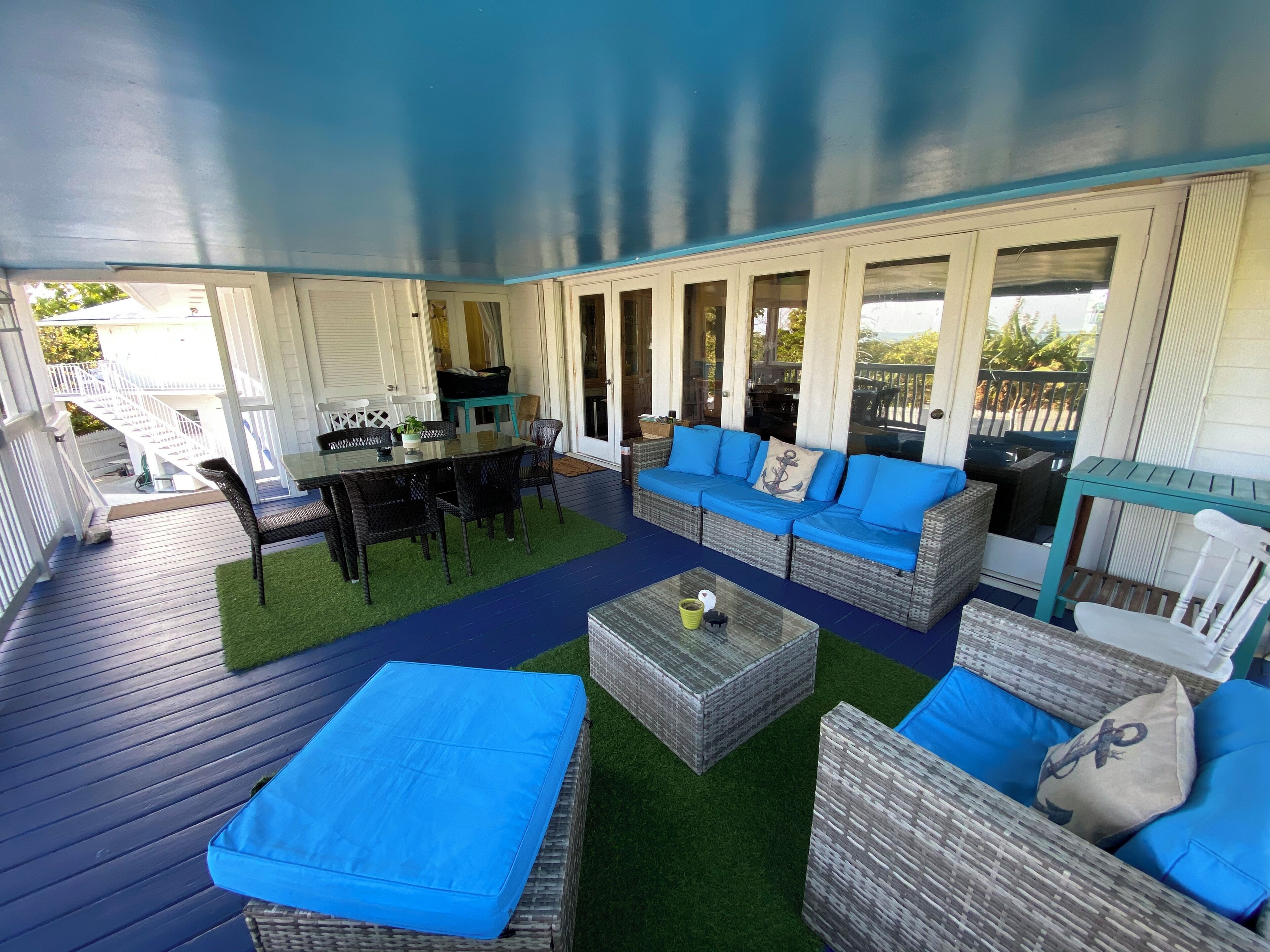A covered outdoor patio with wicker furniture, a glass table, and a blue cushioned sofa.