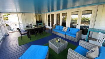 A covered outdoor patio with wicker furniture, a glass table, and a blue cushioned sofa.
