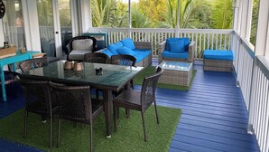A covered outdoor seating area with wicker furniture, a glass table, and a view of lush greenery. - Luxury Oceanview Pool Eco-friendly Villa Near Key West (Summerland Key)