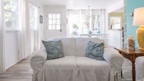 Un salon chaleureux avec un canapé blanc, des coussins à motifs et une petite table en bois sur laquelle est posée une lampe.