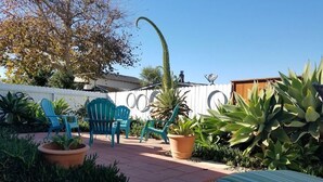 Un espace patio aménagé avec du mobilier d’extérieur, des plantes en pot et une clôture blanche.