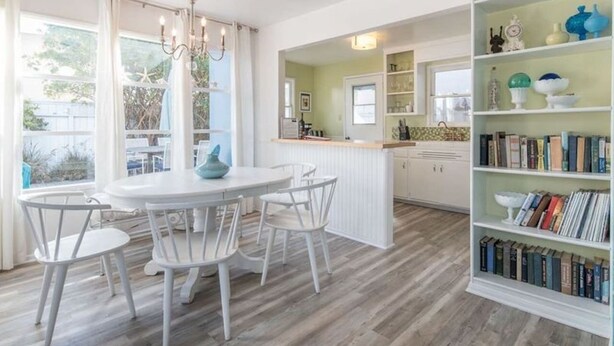 Une cuisine moderne avec des meubles blancs, une table de salle à manger ronde entourée de chaises blanches et une bibliothèque remplie de livres.