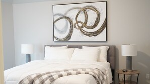 A bedroom with a bed, two bedside lamps, a round table with a lamp, and a wall-mounted abstract painting. - The Cosmopolitan Modern, Cozy, New 3bedroom Home (Yukon)