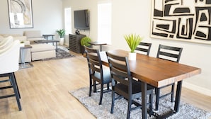 A modern living room with a sofa, coffee table, TV, and dining area with chairs and a table. - The Cosmopolitan Modern, Cozy, New 3bedroom Home (Yukon)