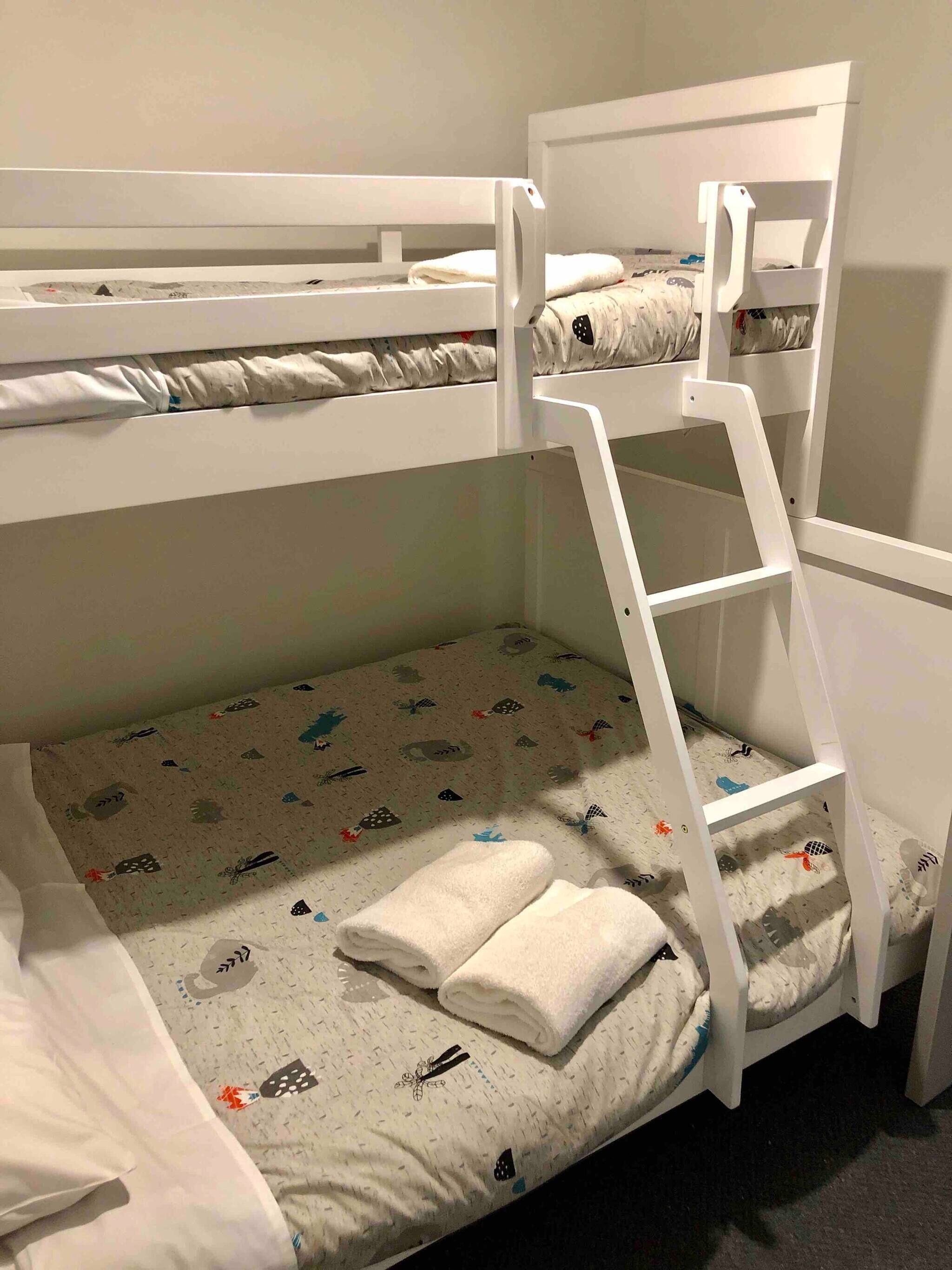 A bunk bed with a ladder, a lower bunk with a patterned mattress, and a top bunk with a plain mattress.