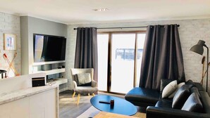A modern living room with a flat-screen TV, a sofa, a chair, and a dining table. - Hotham 3 Bedroom Apt - 24 Lawlers (Hotham Heights)