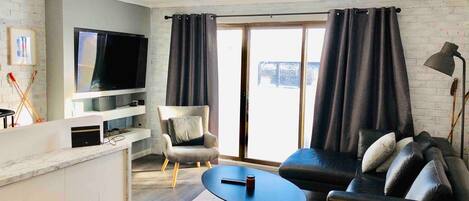 Una sala moderna con una televisión de pantalla plana, un sofá, una silla y una mesa de comedor.