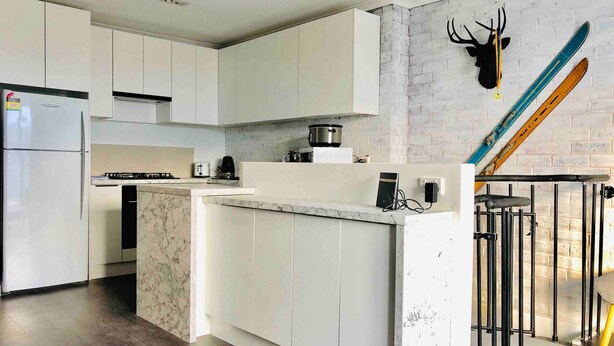 A modern kitchen with white cabinets, a marble island, and a unique deer head decoration on the wall. - Hotham 3 Bedroom Apt - 24 Lawlers (Hotham Heights)