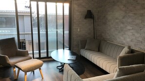 A modern living room with a sofa, two armchairs, a small table, and a floor lamp. Large windows provide a view of the outside. - Hotham 3 Bedroom Apt - 24 Lawlers (Hotham Heights)