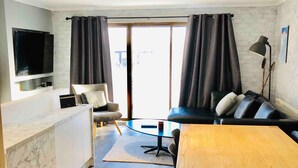 A modern living room with a wooden dining table, black sofa, and a TV mounted on the wall. - Hotham 3 Bedroom Apt - 24 Lawlers (Hotham Heights)