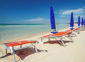 Una spiaggia con file di lettini e ombrelloni blu, acqua cristallina turchese e una riva sabbiosa.