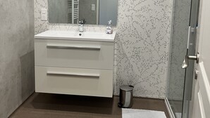 Un baño moderno con un espejo grande, dos lavamanos, un perchero para toallas y una zona de ducha.