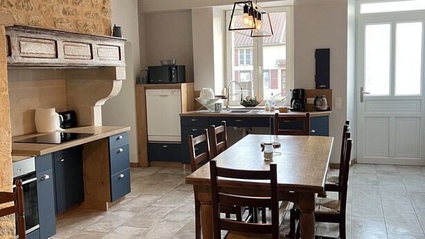 Una cocina amplia con comedor, que cuenta con vigas de madera a la vista, una pared de piedra y electrodomésticos modernos.