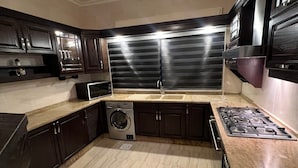 Una cocina con armarios oscuros, una campana extractora de acero inoxidable, lavadora integrada y encimera de granito.