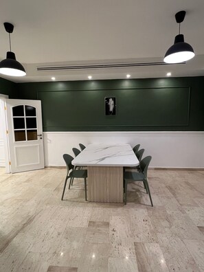 Conference room with a marble-top table and six chairs, surrounded by a green accent wall and recessed lighting.