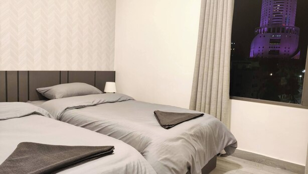 A hotel room with two beds, a nightstand, a lamp, and a window with a view of a building.