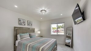 Quarto com cama, luz no teto, janela e televisão na parede.