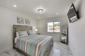 A bedroom with a bed, a ceiling light, a window, and a TV mounted on the wall.