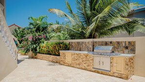 An outdoor kitchen area with a stone wall, a built-in grill, and a stone countertop. - Spacious 4-bedroom Apartment 2 km From Eagle Beach (Noord)