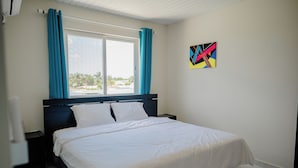 Un dormitorio con una cama, una ventana con cortinas, una mesita de noche y una obra de arte en la pared.