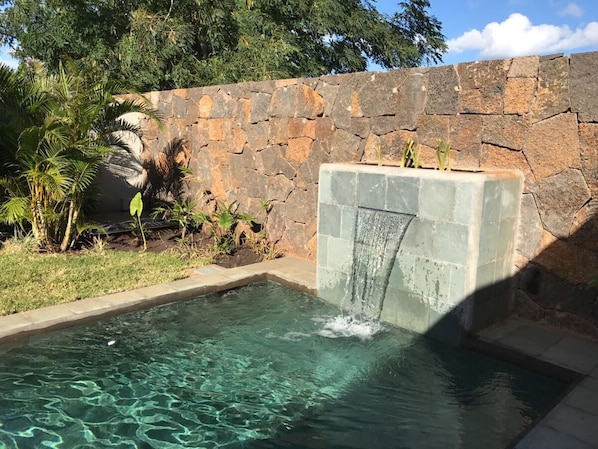 Une piscine avec un mur en pierre et une cascade décorative.