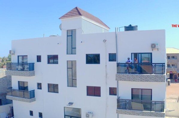 A multi-story residential building with balconies, a water tank on the roof, and a clear sky.
