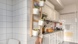 A modern kitchen with white cabinets, a wooden ladder shelf holding potted plants, and a hanging pot rack.