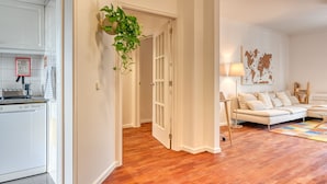 A modern apartment with a kitchen, a living area with a sofa and lamp, and a hallway with a plant.