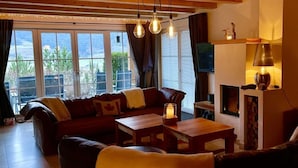 Un salon chaleureux avec un canapé, une table basse et une cheminée. On y trouve également une télévision et une fenêtre avec des rideaux.