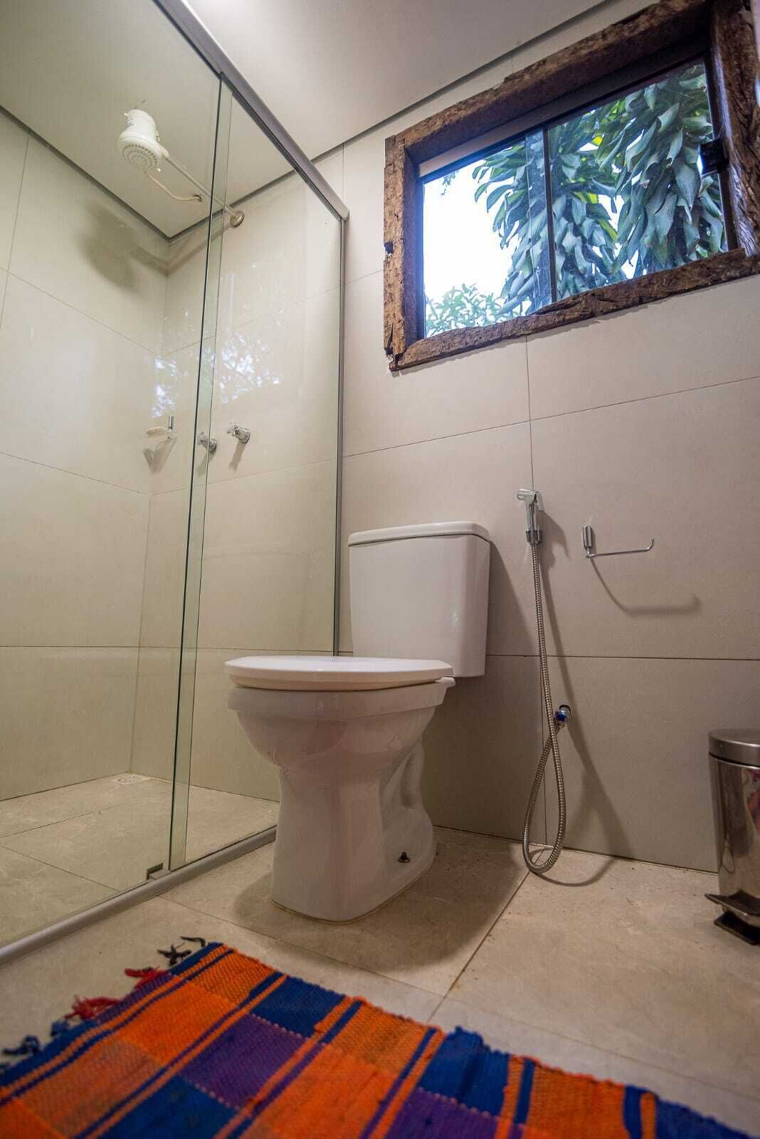 Un baño con cabina de ducha de vidrio, inodoro y ventana con vistas a la vegetación.