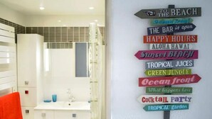 Ein Badezimmer mit einem weißen Waschbecken, einem roten Handtuch und einer Wand mit bunten Schildern, die Annehmlichkeiten wie eine Bar, einen tropischen Garten und eine Cocktailparty kennzeichnen.
