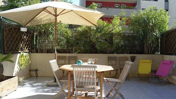 Eine Terrasse im Freien mit einem runden Tisch, vier Stühlen und einem großen Sonnenschirm.