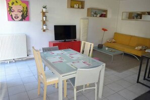 Ein Wohnzimmer mit Esstisch, Stühlen, einer Couch, einem Fernseher und einer Heizung.