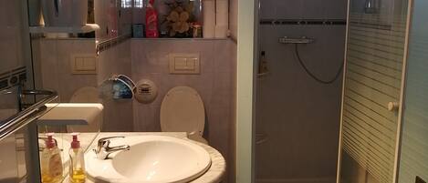 A bathroom with a sink, toilet, and shower. There is a clock on the wall and a mirror above the sink.