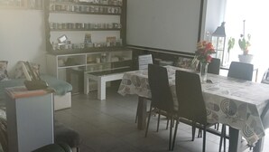 Ein Essbereich mit einem Tisch für vier Personen, einer Couch und einer Bücherwand voller Gegenstände.