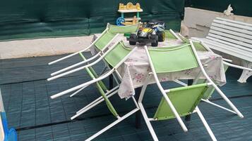 Un espacio exterior techado con una mesa y sillas, un coche de juguete y una maqueta de barco.