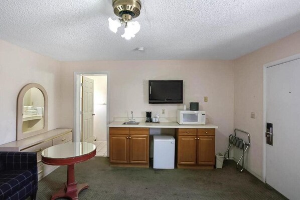 A compact kitchen with wooden cabinets, a microwave, a small refrigerator, and a ceiling fan.
