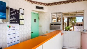 A reception area with a check-in counter, a green door, a wall-mounted AMTEX 2021 calendar, and a window with a view of the outside. - OYO Hotel Yuma AZ - I-8/us-95 (Yuma)
