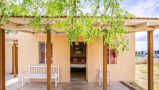 A covered outdoor area with a bench and a chair, a bed visible inside a building, and a clear sky. - OYO Hotel Yuma AZ - I-8/us-95 (Yuma)