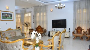 A spacious living room with a large flat-screen TV, elegant furniture, and a chandelier. - 3A Lodge (Lekki)