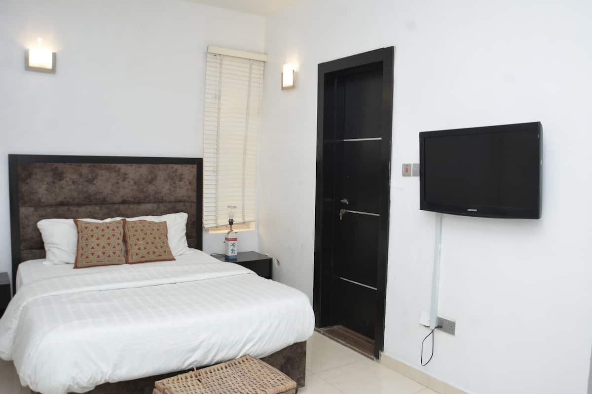 A bedroom with a bed, a nightstand, a television mounted on the wall, and a door.