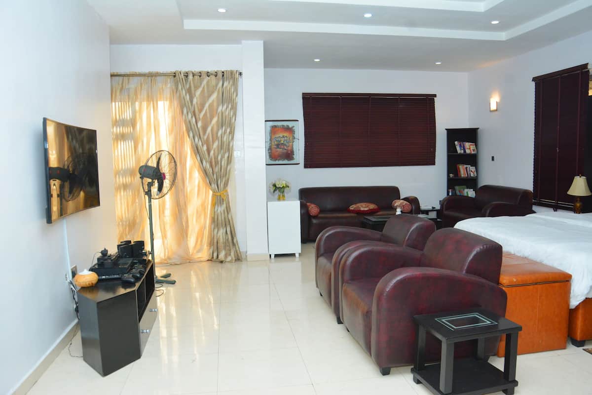 A modern hotel room with a sofa, a bed, a desk with a computer, and a bookshelf.