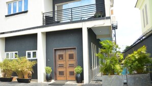 A modern building with a large wooden door, potted plants, and a balcony. - 3A Lodge (Lekki)