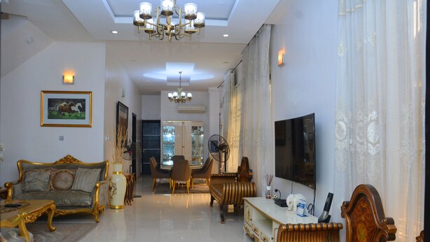 A spacious living room with a sofa, chairs, a coffee table, a TV, and a chandelier. - 3A Lodge (Lekki)