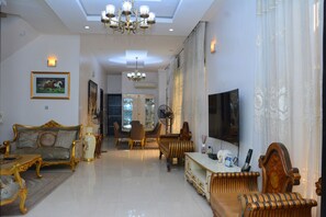 A spacious living room with a sofa, chairs, a coffee table, a TV, and a chandelier. - 3A Lodge (Lekki)
